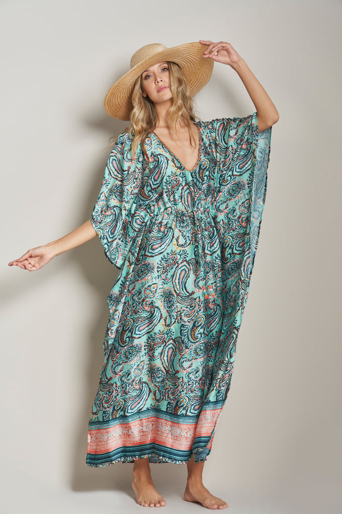 A model standing casually, a bolero on her head, wearing the Shine Eclectic Vibes Kaftan, a long and elegant kaftan adorned in paisley print, with a gathering on the waist.